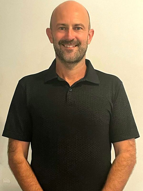 Smiling bald man in black polo shirt against a plain background.
