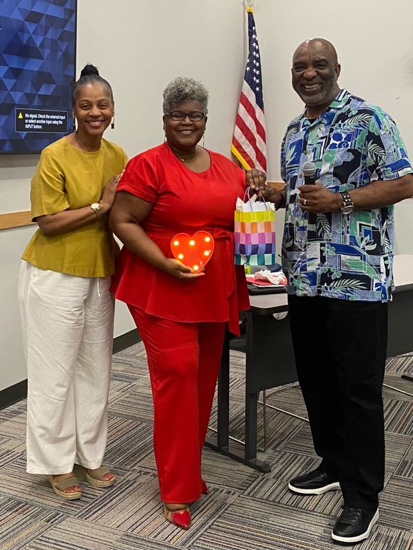 Three people smiling, one holding a lit heart decoration and a gift bag.