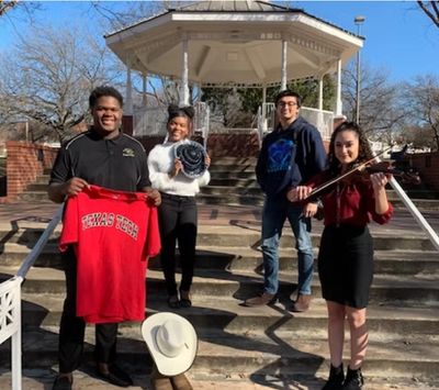 Four young adults pose on outdoor steps, one holding a Texas Tech shirt, another a hat, and another playing a violin.
