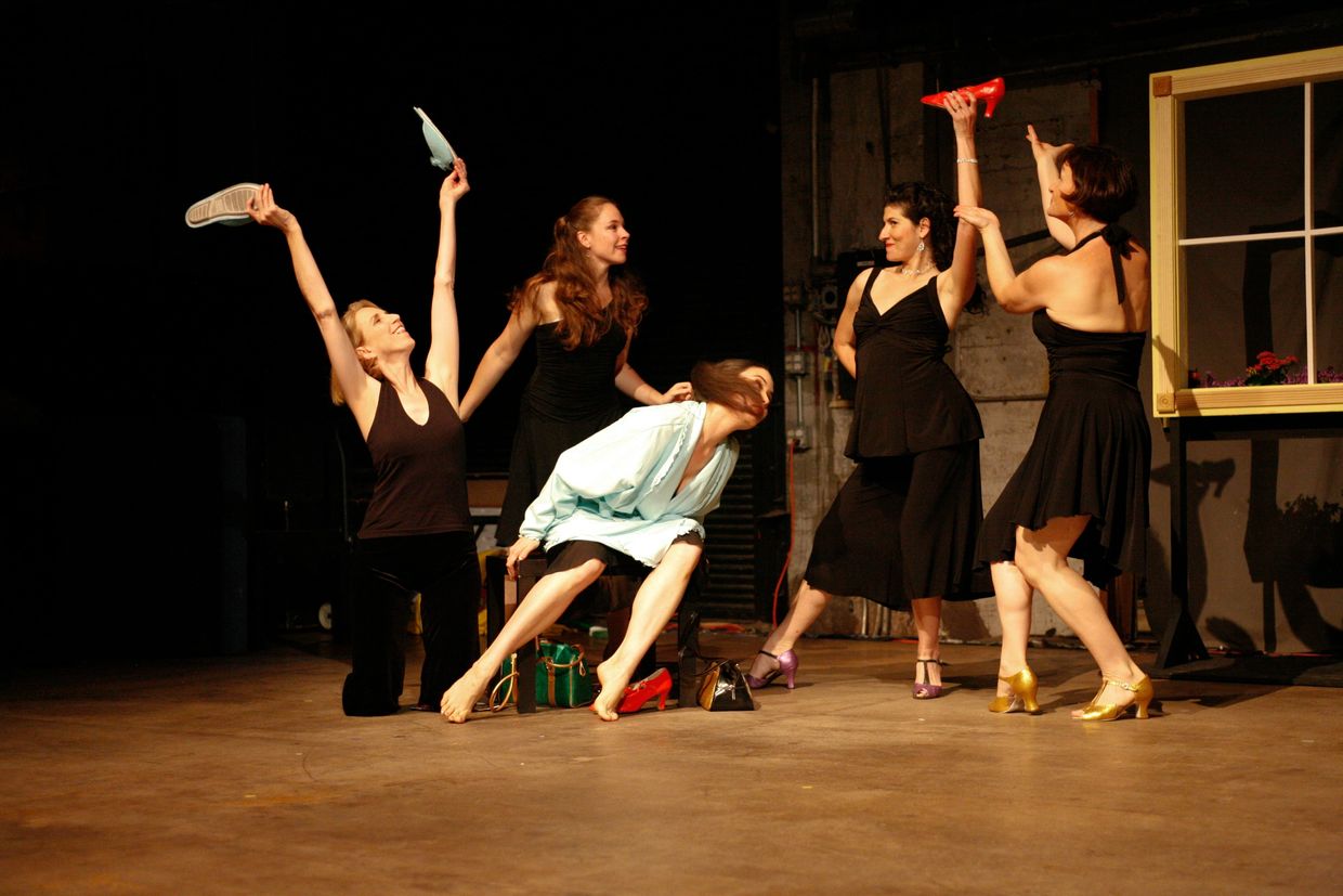 Scene from a performance, group of girls holding up shoes.