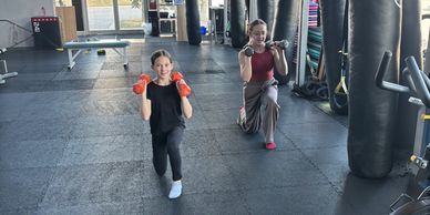 Two females exercising with dumbbells in a gym.