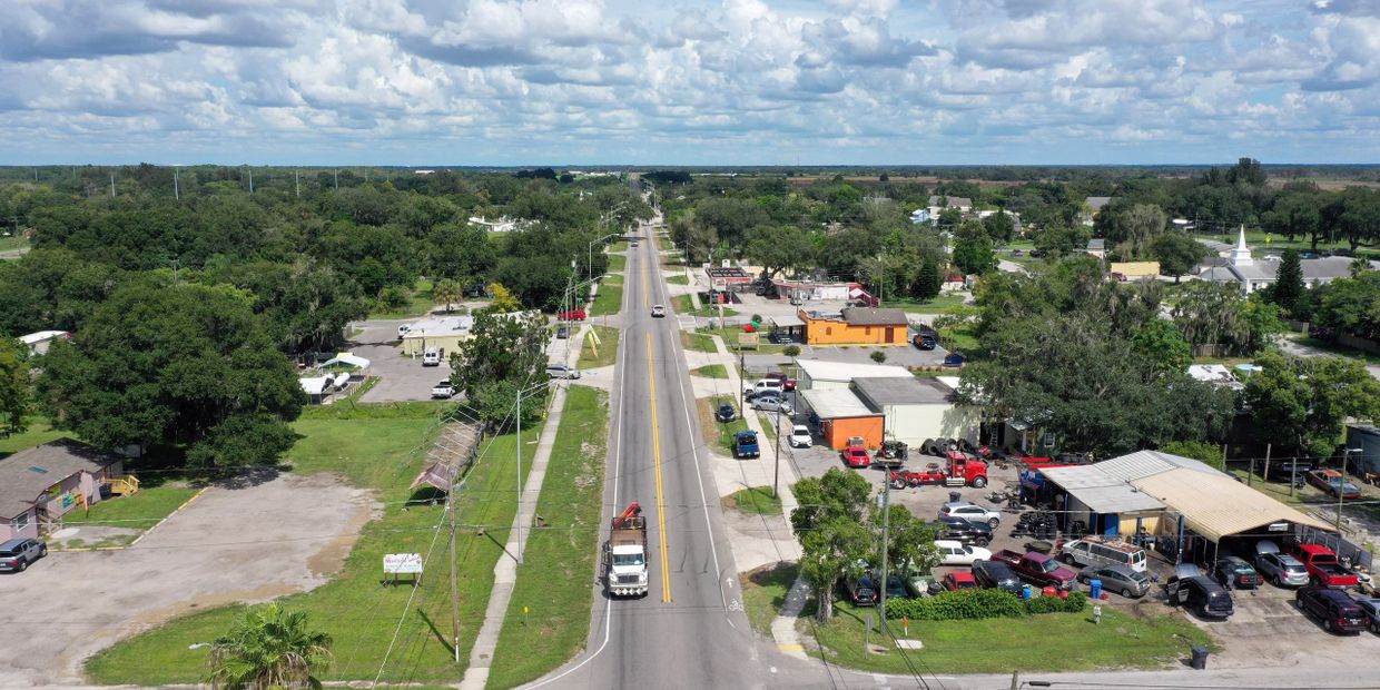 Aerial view of a small town street with vehicles and buildings under a cloudy sky.