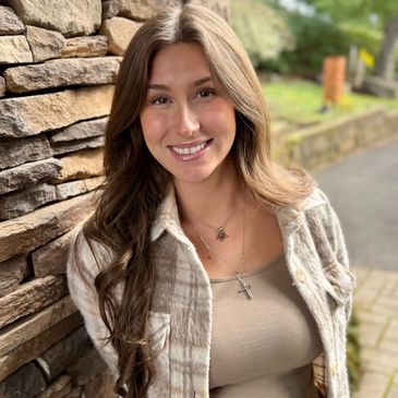 Young woman smiling by a stone wall outdoors.