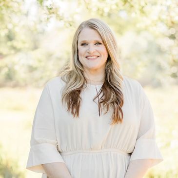 Smiling woman with long blonde hair in a light dress outdoors.