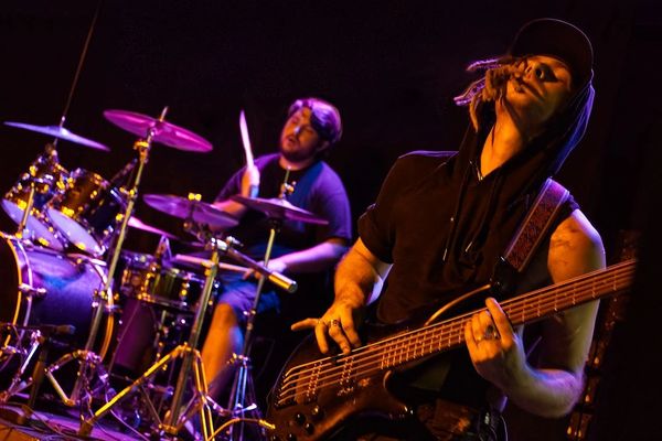 A bassist and drummer passionately playing music on stage with vibrant lighting.