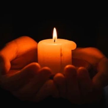 Hands gently holding a lit candle in darkness.