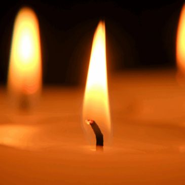Close-up of candle flames glowing warmly in the dark.