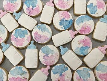Decorated cookies shaped like baby bottles and circles with blue and pink designs.