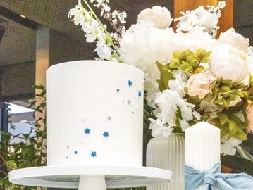 Elegant white cake with blue stars and flowers in the background.