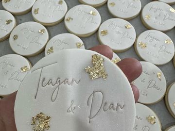 White cookies with names Teagan &amp; Dean and gold accents.