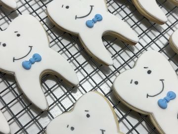 Smiling tooth-shaped cookies with blue bow ties on a cooling rack.