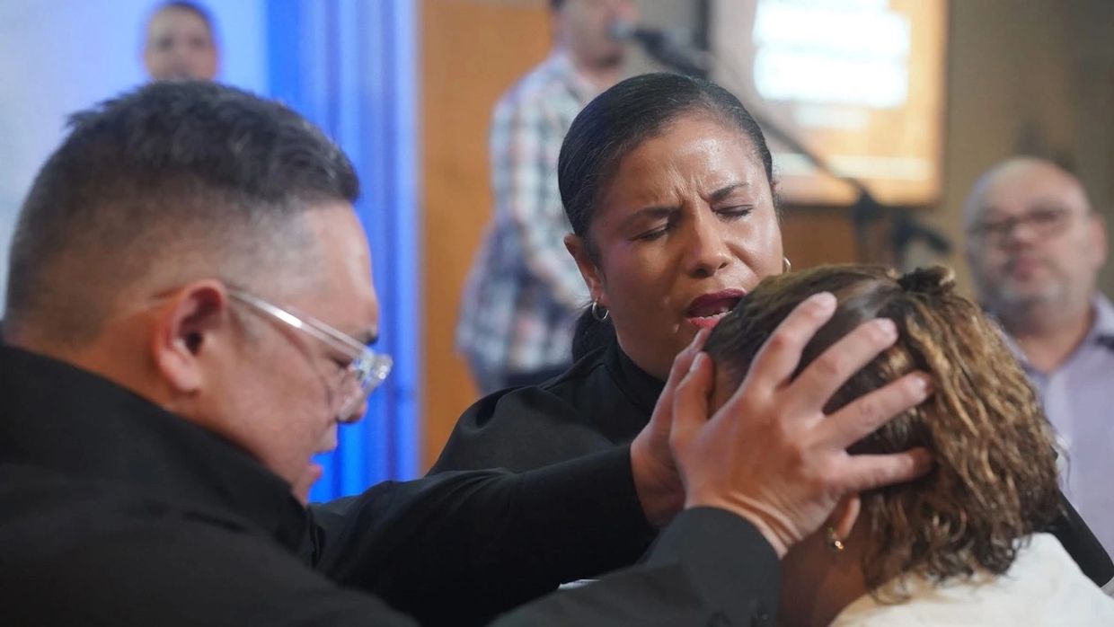 Two people praying over a woman in a spiritual setting.