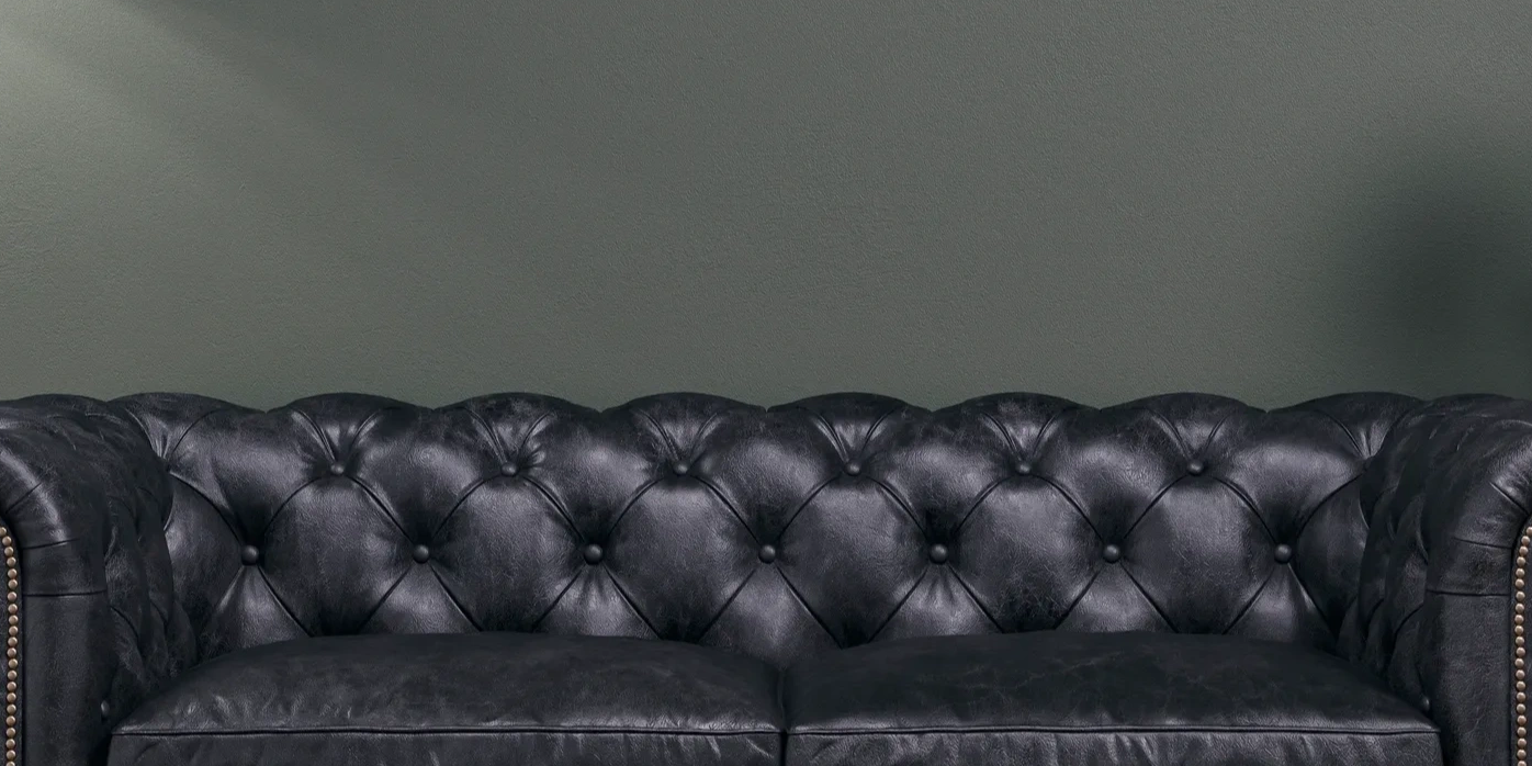 Black leather tufted sofa against a plain wall.