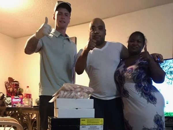 Three people giving thumbs up next to stacked boxes indoors.