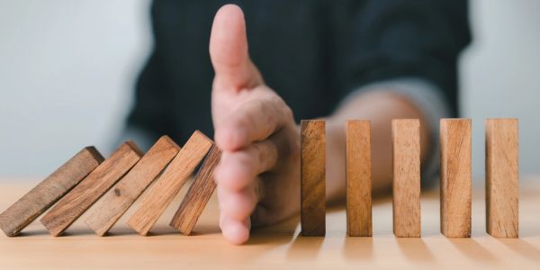 Hand stopping falling dominoes to prevent a chain reaction.