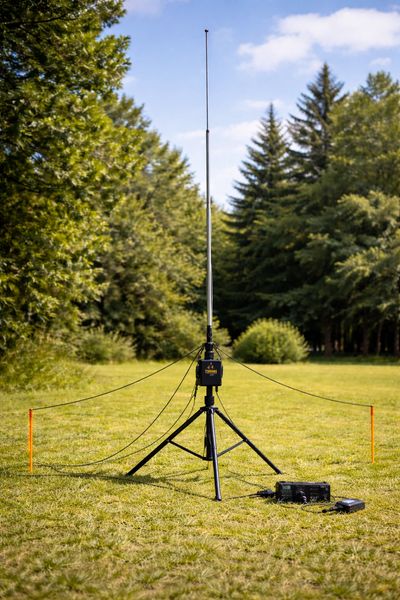 Portable radio antenna setup on grassy field surrounded by trees.