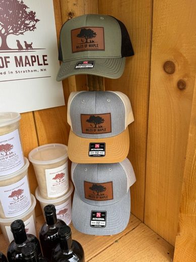 Three 'Miles of Maple' branded caps displayed on a wooden shelf.