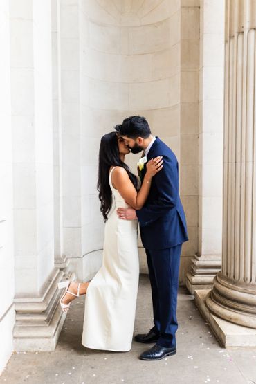 A bride and groom share a kiss in an elegant architectural setting.