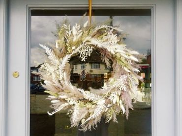A decorative wreath made of dried white and beige foliage hanging on a glass door.