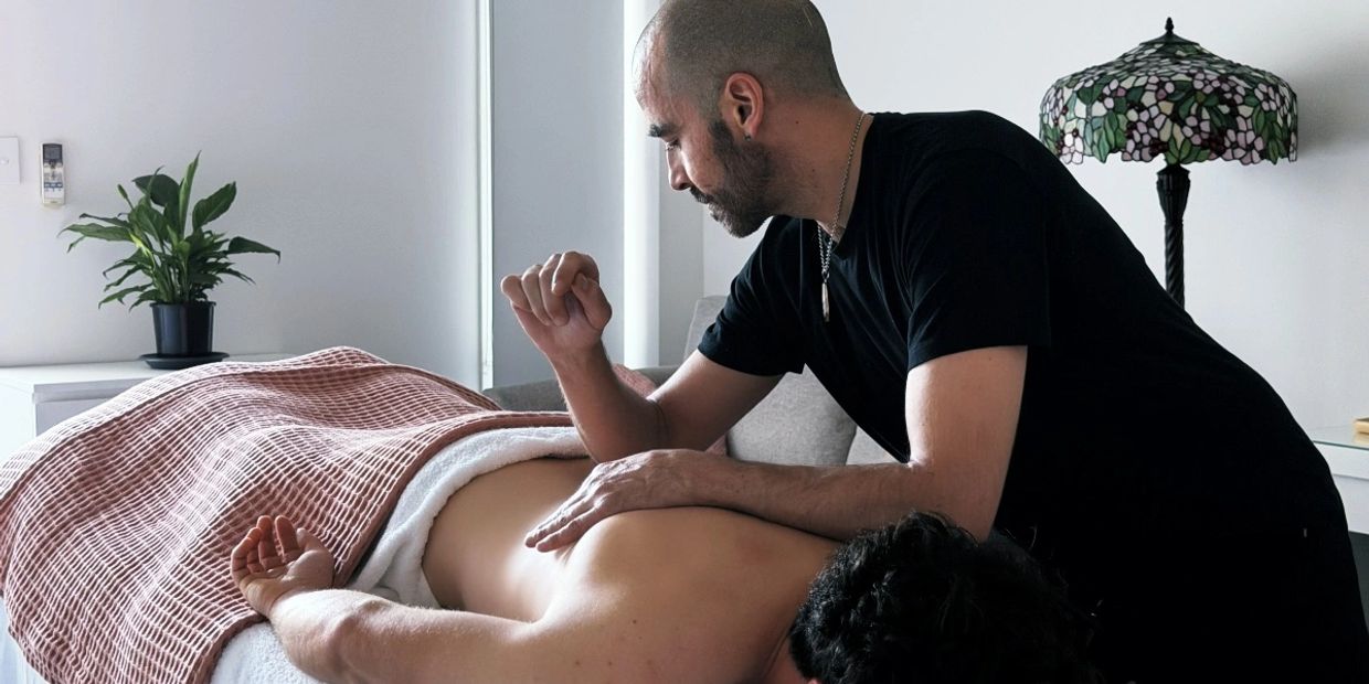 A man is giving a back massage to a person lying face down under a blanket.