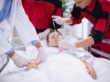 Medical team attending to an unconscious child in a hospital bed.