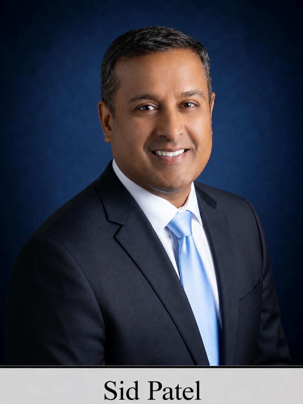 Professional headshot of Sid Patel in a suit and light blue tie.