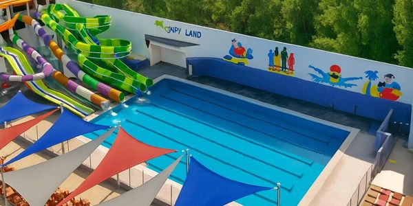 Colorful water slides beside a clear blue pool under vibrant shade sails.