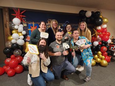 Group of friends posing with Las Vegas-themed props and balloons.