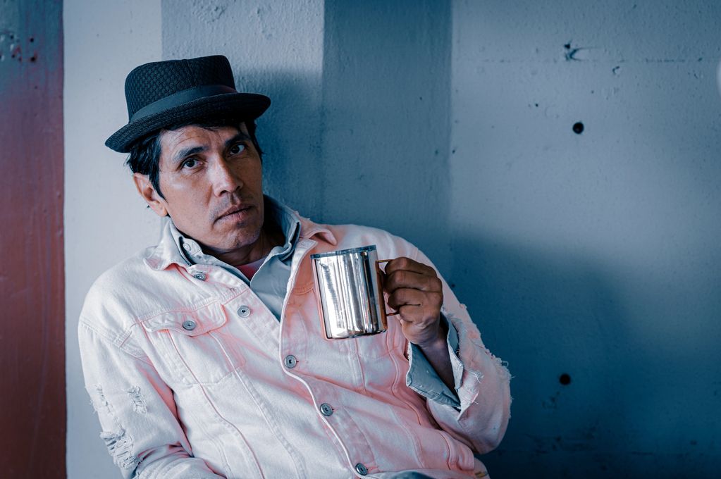 Man in a hat holding a metallic mug, wearing a light jacket.