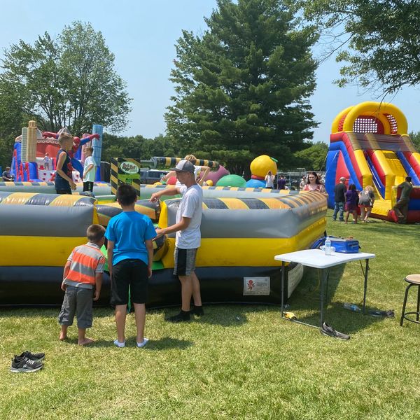 Kids enjoying inflatable games at an outdoor event on a sunny day.