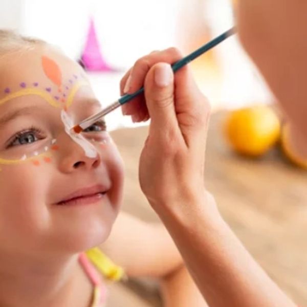 A child smiling while getting face paint applied.