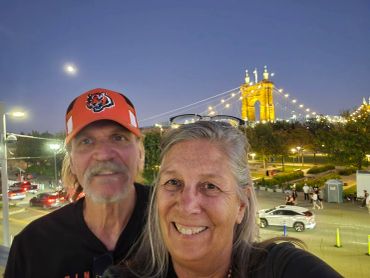 A smiling couple with a lit bridge in the background at dusk.