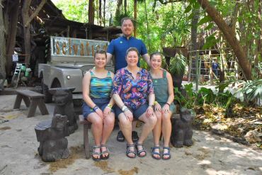 A happy family sitting on a bench outdoors surrounded by greenery and stone animal sculptures.