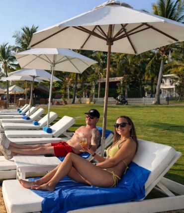 A couple relaxing on beach loungers under umbrellas on a sunny day.