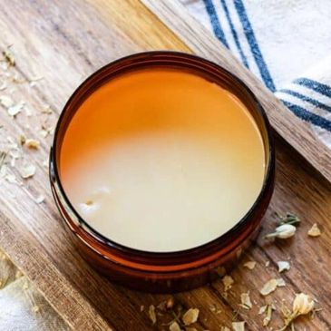 A brown jar of tallow balm on a wooden tray with scattered lemon myrtle.