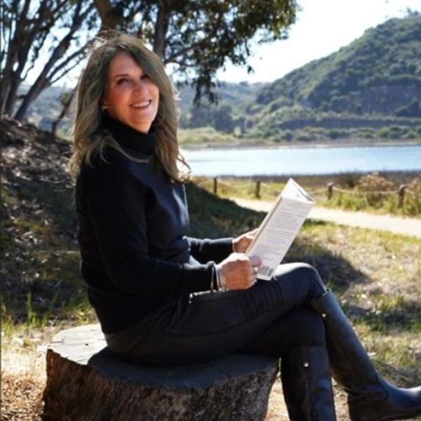 Woman sitting on a tree stump reading a book outdoors.