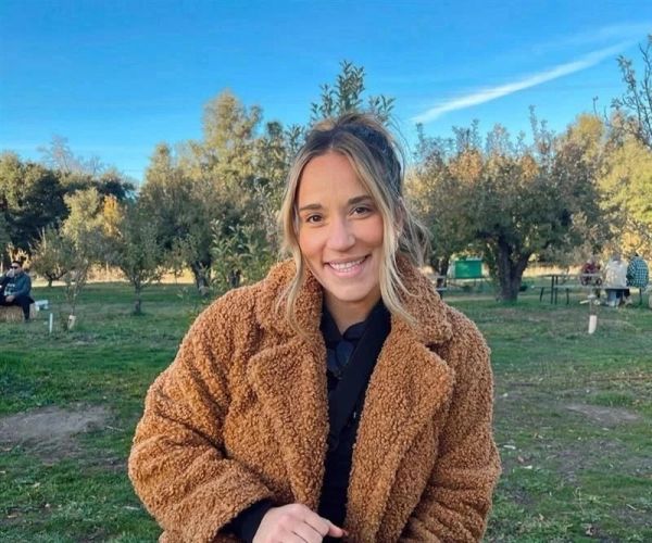Smiling woman in a brown coat outdoors.