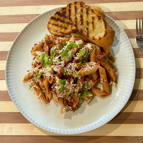 Plate of penne pasta with tomato sauce, grated cheese, garnish, and grilled bread.