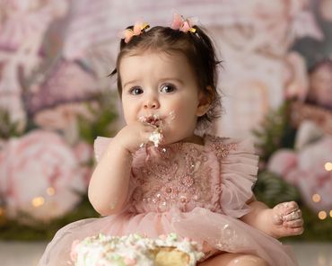 Fairy cake smash session  little girl eating cake and licking fingers during her studio cake smash.
