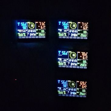 Four illuminated weather station displays showing temperature, humidity, and other data in the dark.