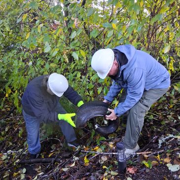 Two workers in helmets removing tires from a wooded area.
