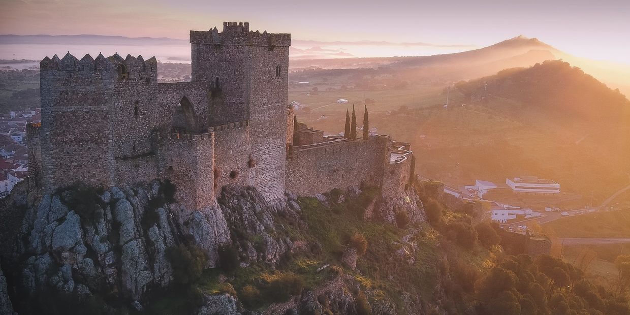 Ancient stone castle perched on rocky hill at sunrise.