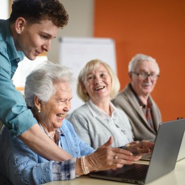 Someone helping 3 active adult seniors with computers 