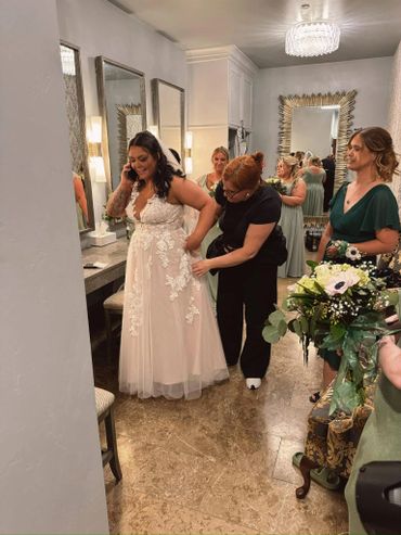 Bride getting ready with help in a dressing room before the wedding.