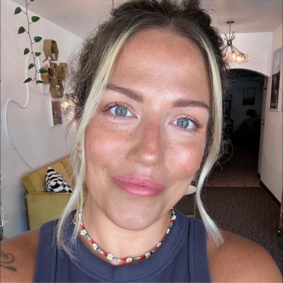 Close-up of a smiling woman with blue eyes and a floral necklace indoors.