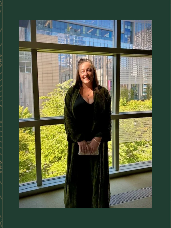 Woman in black dress smiling by large window with city view.