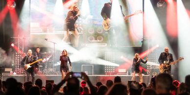 A live band performs energetically on stage with bright lights and an enthusiastic audience.