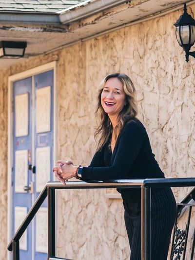A smiling woman leaning on a railing outside a textured wall building.