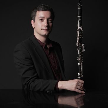 Man in black suit holding a clarinet, posing against a dark background.