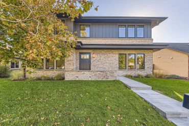 Modern two-story house with stone facade and large windows.
